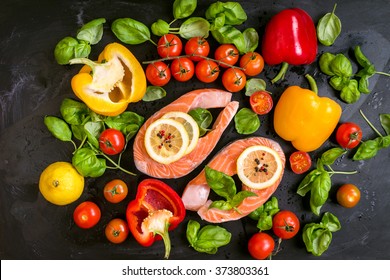 Raw salmon steaks with lemon slices and fresh cherry tomatoes, bell pepper, basil leaves and dry pepper. Ingredients for cooking on a dark background. Healthy and diet food concept. Top view - Powered by Shutterstock