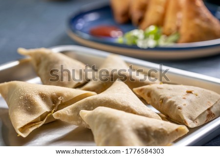 Raw samosa wraps are ready to be fried placed in front of few cooked samosas