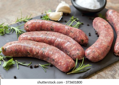 Raw sausages on slate, with herbs and spices. Side view.