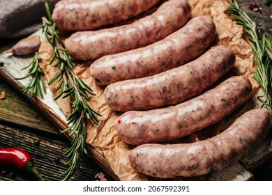raw sausages with rosemary on a wooden background. Sausages for grilling. Food recipe background. Close up.