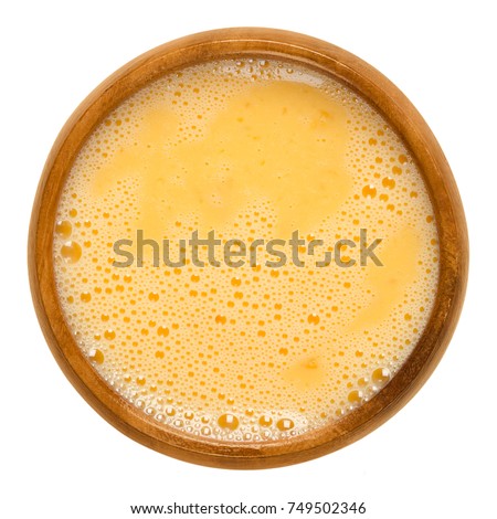 Raw scrambled eggs in wooden bowl. Yolk and white are stirred together and ready for further processing. Used for pancakes, omelettes or for breading. Macro food photo close up from above over white.