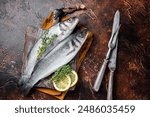 Raw Sea Bass, Branzino fish with thyme and lemon. Dark background. Top view.