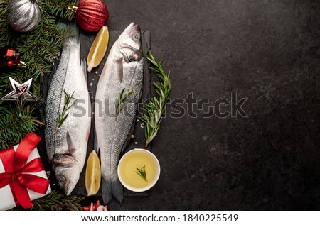 Raw sea bass fish with spices for the Christmas holiday on a stone background with a Christmas tree and new year toys with copy space