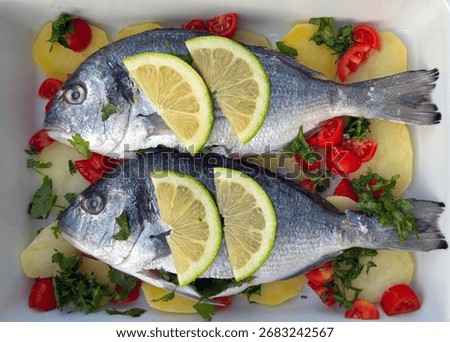 Raw sea bream fish with lemon slices, potatoes, tomatoes and parsley in baking tray