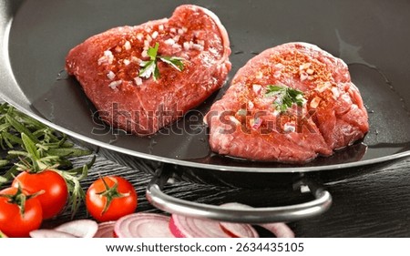Raw seasoned piece of raw meat prepared for cooking, placed on a kitchen table surrounded by fresh ingredients and herbs  – healthy cooking and lifestyle concept. 