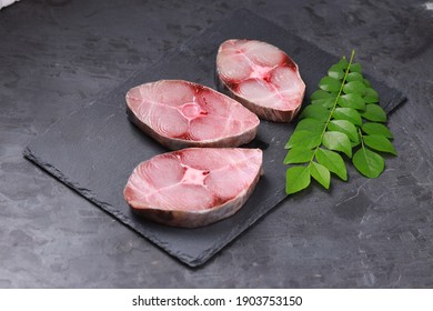 Raw Seer fish or Ayakura ,steaks of seer fish arranged on a graphite slate with grey colour background and garnished with fresh curry leaves ,isolated images.