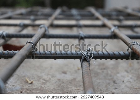 Raw shot featuring rust rebar fixed with thin wire, creating a grid pattern on concrete surface, and blurred background. Focus is on the foreground material.