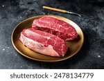 Raw Shoulder Top Blade beef meat steaks on a plate. Black background. Top View.