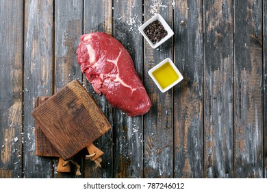 Raw Sirloin Steak Over The Rustic Wooden Board Decorated With Sea Salt, Black Pepper, Olive Oil . Top View. Copy Space