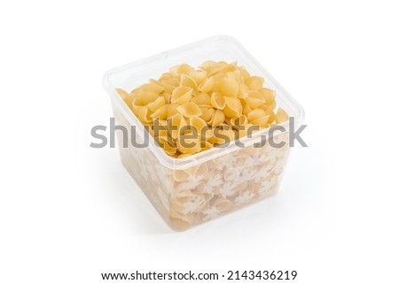 Raw small seashells shaped pasta also known as conchiglie or conchigliette in the translucent square plastic container on a white background
