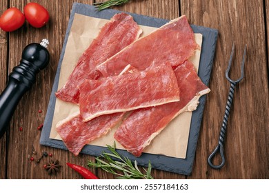 Raw smoked pork chips on a stone tray with vegetables and spices on a wooden table, top view of a fresh beer snack - Powered by Shutterstock