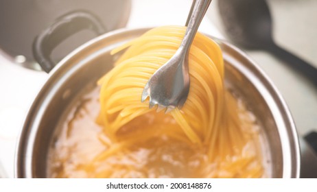 Raw spaghetti is being cooked in boiling water in a kitchen pot. Healthy Italian Food and Cooking concepts.