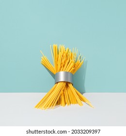 Raw Spaghetti And Duct Tape Roll Composition Against Cyan Blue Background. Abstract Yellow Pasta With Grey Adhesive Tape Creative Concept. Surreal Italian Food Art Direction.