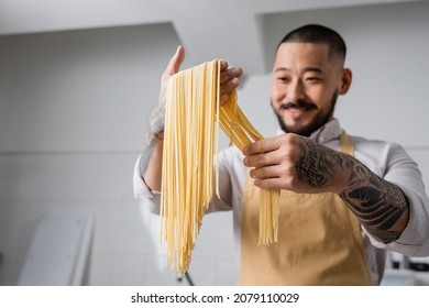Espaghetti crudo en manos de un alegre chef asiático en la cocina