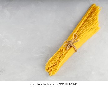 Raw spaghetti tied with twine on gray background. Yellow uncooked pasta spaghetti on concrete. Top view. Copy space - Powered by Shutterstock