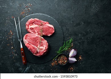 Raw Steak Ribeye Black Angus with a fork on a black stone background. Top view. free space for your text. Rustic style. - Shutterstock ID 1593810973