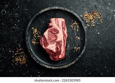 Raw Steak Ribeye Black Angus on a wooden plate ready to be cooked. On a black stone background. Rustic style. - Shutterstock ID 2265303985