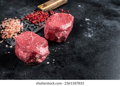 Raw steaks fillet Mignon on a butcher cleaver. Beef tenderloin. Black background. Top view. Space for text. - Powered by Shutterstock