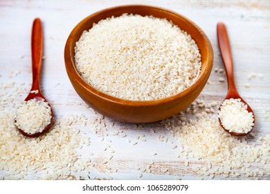 Raw  steamed rice in a bowl and two spoons on a wooden background. Ingredient for a healthy diet.