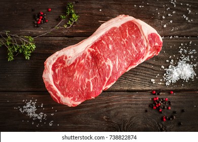 raw strip loin steak on white wooden background in rustic style with salt and herbs