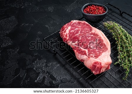 Raw striploin or New York beef meat steak ready for BBQ. Black background. Top view. Copy space