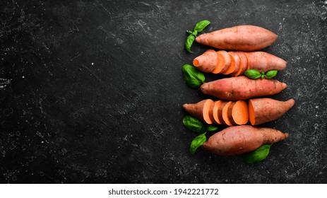 Raw Sweet Potatoes And Basil On A Black Stone Background. Top View. Free Space For Your Text.