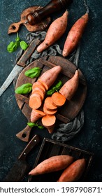 Raw Sweet Potatoes And Basil On A Black Stone Background. Top View. Free Space For Your Text.