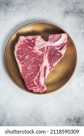 Raw T-bone Porterhouse Beef Meat Steak On Golden Metalic Plate. Gray Background. Top View