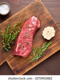 Raw Tender And Marbled Striploin Steak With Salt, Garlic Clove And Spices Rosemary And Thyme On Wooden Board. Uncooked Sirloin Beef. Preparation For Cooking. Vertical, Overhead