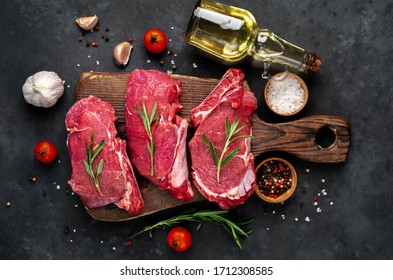 
raw three beef steaks on a cutting board with spices on a stone background - Powered by Shutterstock