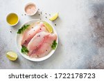 Raw tilapia fillet with lime and spices on a gray stone background. Flat lay. Copy space