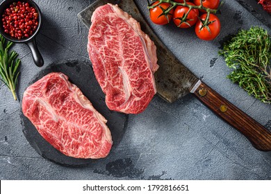 Raw Top Blade Oyster Steak On Stone And Meat Butcher Cleaver, Marbled Beef With Herbs Tomatoes Peppercorns Top View