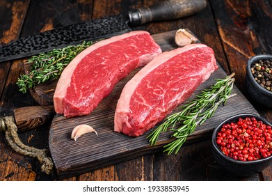 Raw top sirloin beef meat steak on a cutting wooden board. Dark wooden background. Top view.