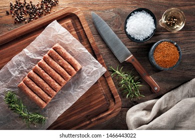 Raw Turkish Inegol Meatballs On White Cooking Paper And Wooden Table. Decorated With Salt, Pepper, Meat Knife And Napkin. Overhead View.