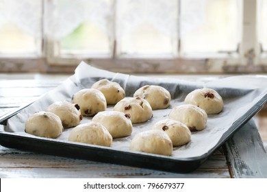 Raw unbaked buns. Ready to bake homemade Easter traditional hot cross buns on oven tray with baking paper over white wooden table with window at background. Natural day light. Rustic style.