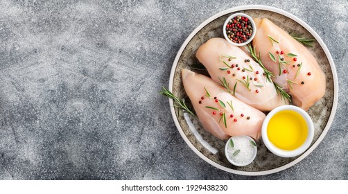 Raw uncooked chicken breasts with spices and herbs on gray concrete table, chicken meat with ingredients for cooking. Top view