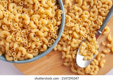 Raw or uncooked Elbow Pasta in a blue bowl and on a wooden choppin board with a spoon on the side top view, flat lay or overhaed shot.