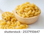 Raw uncooked macaroni in a wooden bowl on a white background	