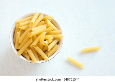 Raw Uncooked Pasta Penne In Bowl Over White Wooden Background