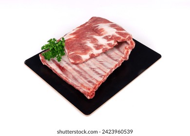 A raw, uncooked, rack of pork spare ribs with parsley garnish on a black plate isolated on white - Powered by Shutterstock