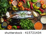Raw uncooked seabass fish with vegetables, grains, herbs and spices on chopping board over rustic wooden background, top view