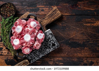 Raw veal beef Oxtail Meat on butcher wooden board with cleaver. Dark wooden background. Top view. Copy space