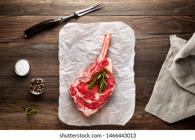 Raw Veal Rib Chop On White Cooking Paper And Wooden Table. Decorated With Salt, Pepper, Meat Fork And Napkin. Overhead View.