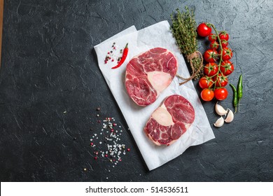 Raw veal shank slices meat and ingredients for Osso Buco cooking on black background, top view