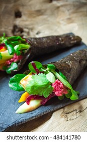 Raw vegan nori hand rolls with pink horseradish sauce, salad and vegetables. On a slate plate against a wooden background. Vegetarian, gluten-free food.