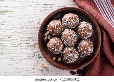 Raw vegan sweets, energy balls with dried fruits and coconut. Brown plate with a napkin. Top view