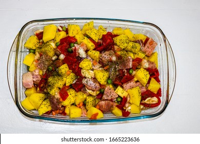 Raw vegetables ( potatoes, carrots, green peas, red pepper and onion) with pork meat garlic and spices in pyrex tray prepared for cooking in the oven.