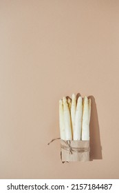 Raw white asparagus in a bundle tied with paper and string. Top view with copy space on plain brown background. Light with harsh shadows.