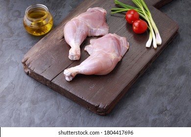 Raw Whole Chicken Leg Without Skin Arranged In A Wooden Base And Garnished With  Small Tomato Or Cherry Tomato ,spring Onion And Cooking Oil ;ingrediants   On Grey Or Graphite Texture