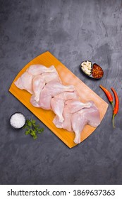 Raw Whole Chicken Leg Without Skin Arranged In A Wooden Base And Garnished With Chilli Flakes, Garlic, Red Chilli,coriander Leaf And Salt On Grey Or Graphite Texture